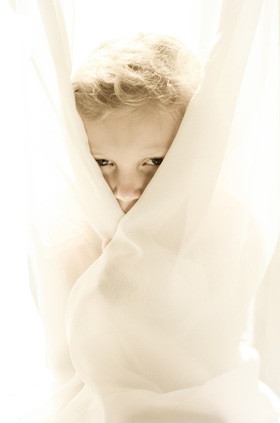 eyes of little blond girl hiden by curtain - 写真・画像
