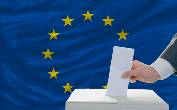 Мужчина голосует на выборах в Европе перед флагом
 - Фото, изображение