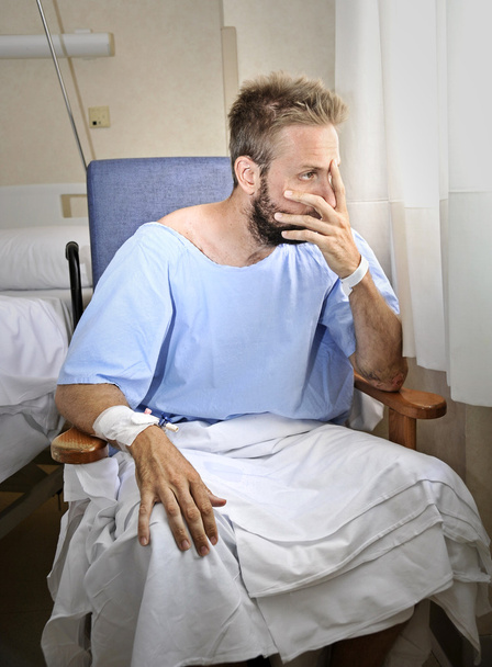 молодой раненый мужчина в больничной палате сидит в одиночестве от боли, беспокоясь о своем состоянии здоровья
 - Фото, изображение
