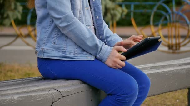 Chica joven sentada en el banco y usando tableta PC, parcialmente visto
 - Metraje, vídeo