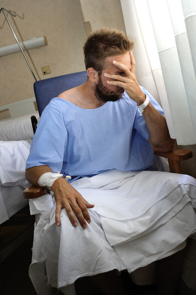 young injured man crying in hospital room sitting alone crying in pain worried for his health condition - Photo, Image
