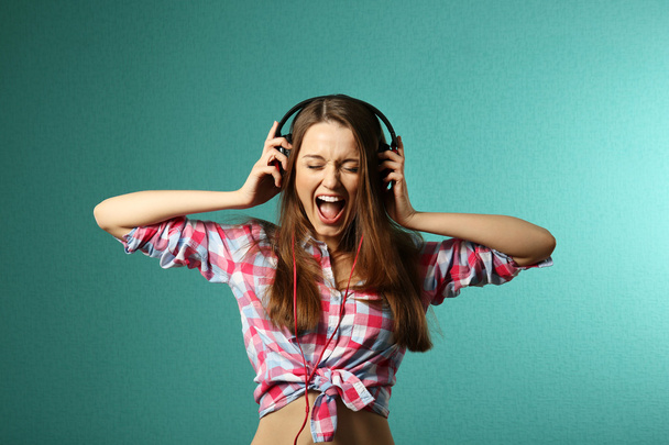 Young woman with headphones on turquoise background - Photo, image