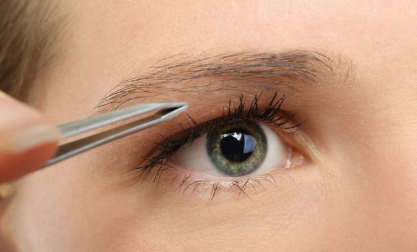Junge Frau zupft Augenbrauen mit Pinzette aus nächster Nähe - Foto, Bild