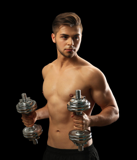 Muscle young man holding dumbbells on dark background - Foto, Imagem