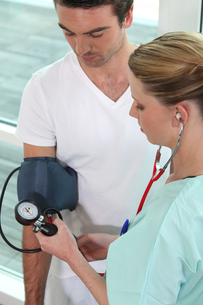 Young nurse taking blood pressure of a man - Фото, зображення