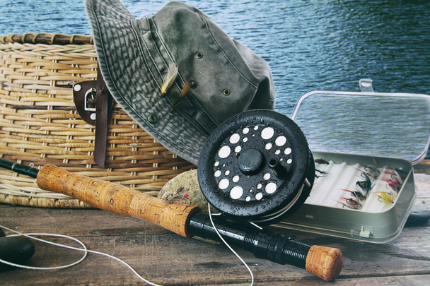 Sombrero y artes de pesca con mosca en la mesa cerca del agua
 - Foto, Imagen