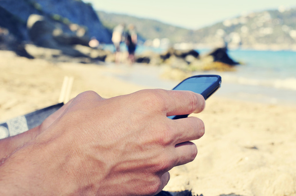 young man using a smartphone on the beach - 写真・画像