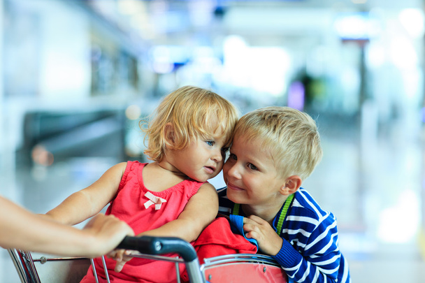happy kids at airport riding on luggage cart - Zdjęcie, obraz