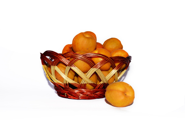 abrikozen in rieten mand op witte achtergrond - Foto, afbeelding