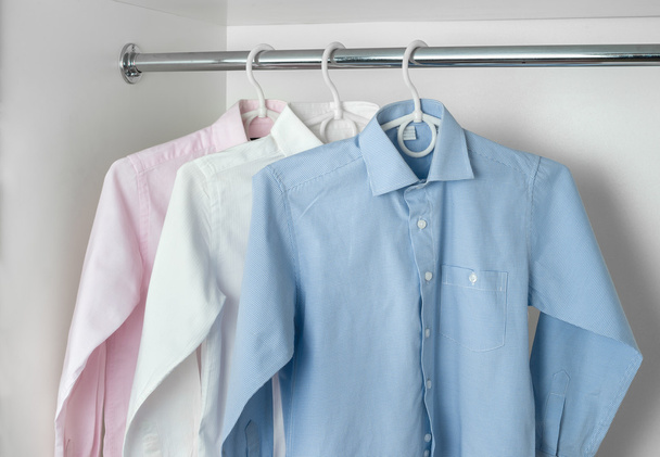 Camisas planchadas limpias blancas, azules y rosas para hombre que cuelgan de la percha
 - Foto, imagen