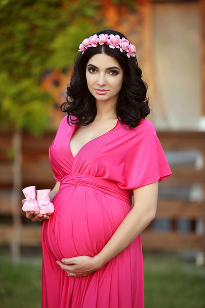 Beautiful pregnant woman holding baby's bootee wearing in pink d - Foto, imagen