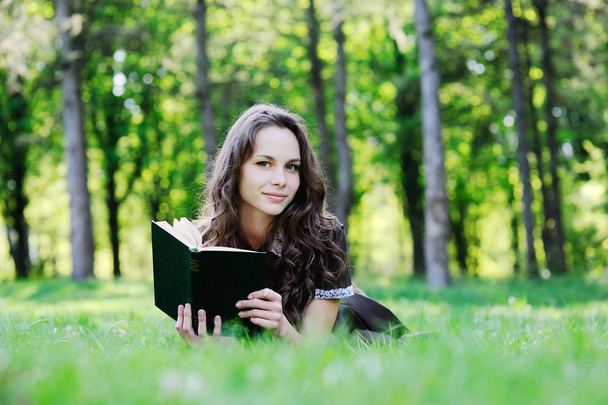 Schoolgirl reading a book sitting on the grass. Beautiful girl reading a book - Fotografie, Obrázek