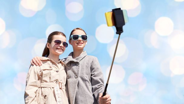 happy girls with smartphone selfie stick over blue - Фото, зображення