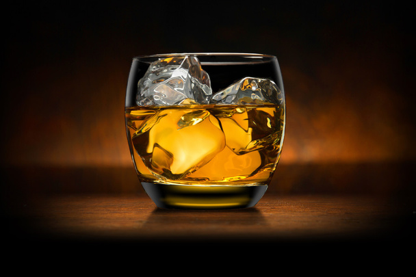 Single glass of whisky whiskey bourbon on ice on top of a wood bar table and wooden background - Foto, imagen