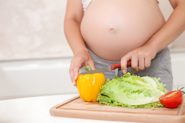 Young pregnant woman is making a salad in kitchen - Foto, Imagen