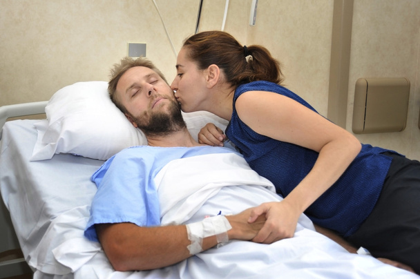 思いやりのある彼の手を握ってベッドの心配女性の横になっている病院の部屋の人で若いカップル - 写真・画像