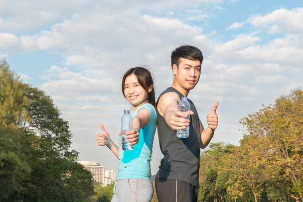 Giovane asiatico uomo e donna bere acqua da una bottiglia e pollice
 - Foto, immagini