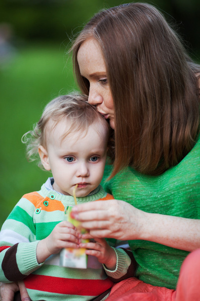Madre besando al niño bebiendo jugo al aire libre
 - Foto, Imagen