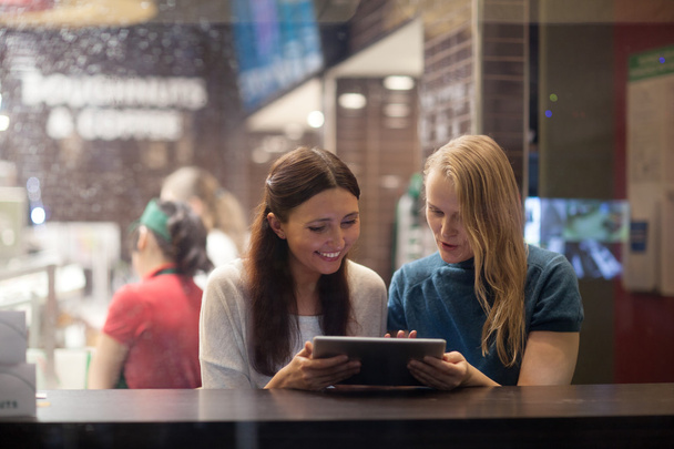 Δύο γυναίκες μιλούν χαρούμενα στο εστιατόριο χρησιμοποιώντας ηλεκτρονική ταμπλέτα - Φωτογραφία, εικόνα