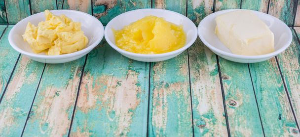 ein Block Butter, Margarine und Ghee in weißen Schalen vor rustikalem Holzhintergrund - Foto, Bild
