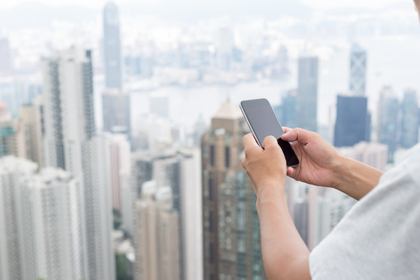 рука держит мобильный телефон с городским пейзажем в качестве фона
 - Фото, изображение