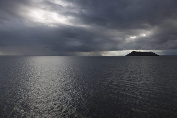 dunkle und düstere Stimmung aufgrund von Regenschauern und bedrohlichem Himmel in der Nähe der Insel Daphne, wodurch die Insel fast wie eine Silhouette erscheint. - Foto, Bild