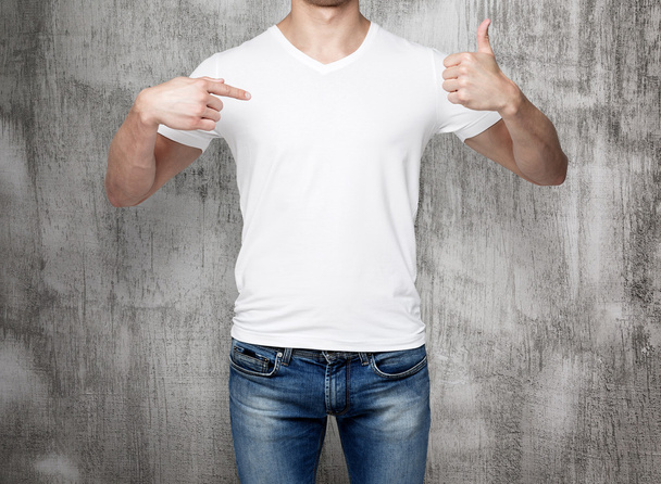Close-up of a man pointing his finger to a blank t-shirt, and the thumb up. Concrete background. - Foto, Imagem
