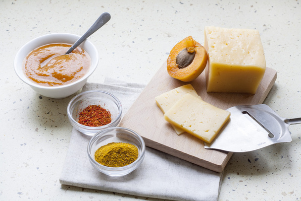 Kiinteä viipaloitu juusto, jossa on aprikoosicurrya keraamisissa tavaroissa, mausteissa ja tuoreissa aprikooseissa, valikoiva
 - Valokuva, kuva