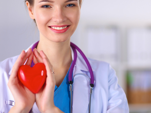 Genç bir kadın doktor elinde kırmızı bir kalp, hastanede duruyor. - Fotoğraf, Görsel