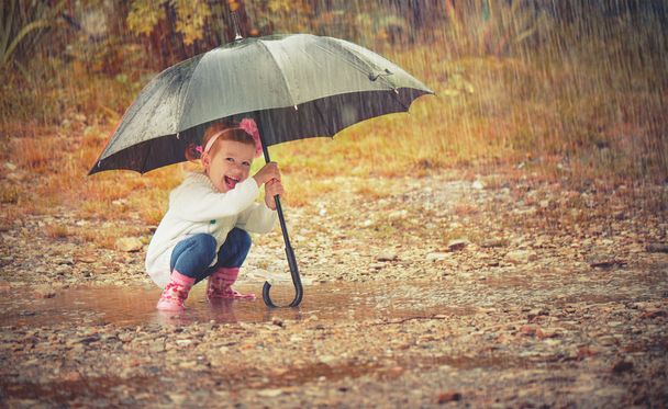 happy baby girl with an umbrella in the rain playing on nature - Photo, Image