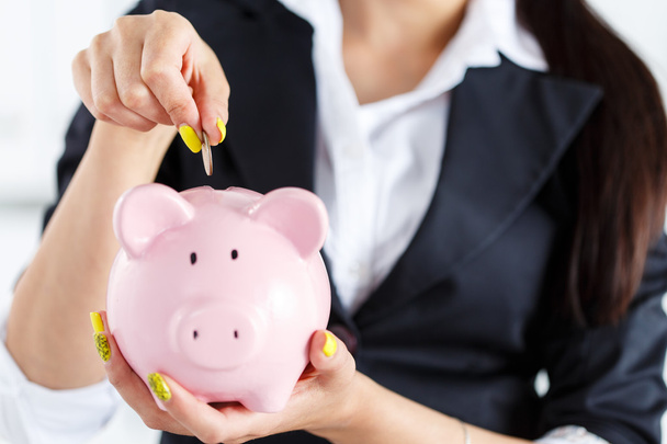 Business woman putting pin money coins into pink piggybank slot - Foto, afbeelding