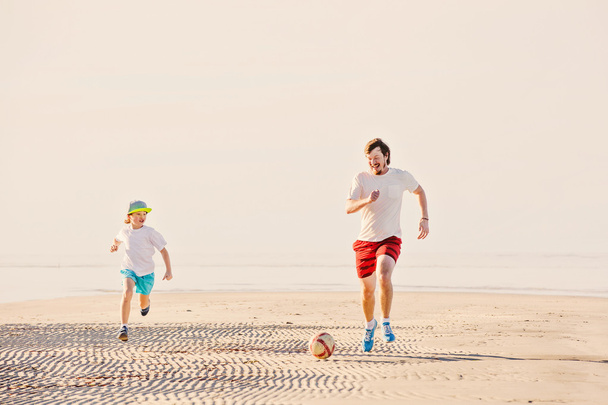 Ευτυχής πατέρας και γιος παίζουν ποδόσφαιρο ή το ποδόσφαιρο στην παραλία - Φωτογραφία, εικόνα