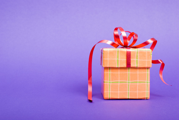 Single orange gift box with red ribbon on blue background. - Foto, imagen