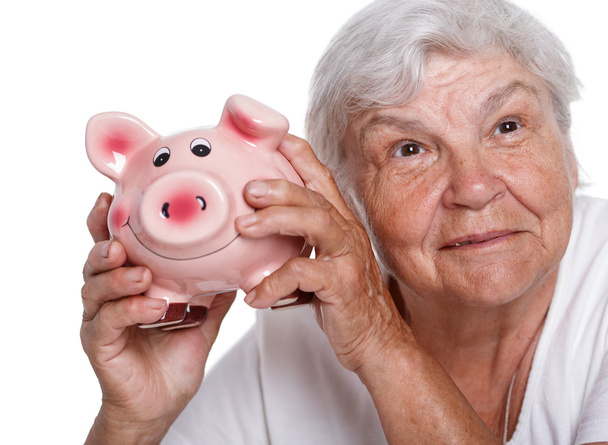 Elder woman holding and hugging funny pink piggybank. Budgeting expenses, making savings, effective investment concept. Future needs deposit. Focus on pig. Retirement and retiree finansial problems - Fotoğraf, Görsel