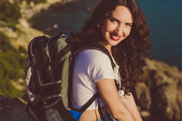 Happy girl with backpack is sitting on rock peak  - Fotó, kép