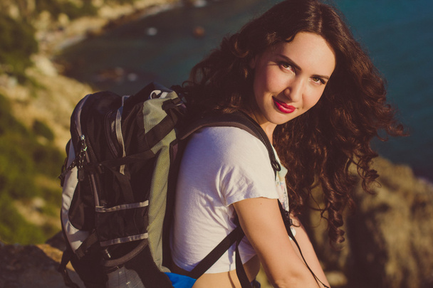 Chica feliz con mochila está sentado en pico de roca
  - Foto, Imagen