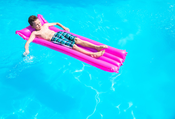 A boy floats on an inflatable mattress in the pool - Фото, зображення