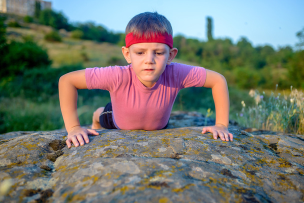 Jeune garçon faisant des pompes sur un rocher
 - Photo, image