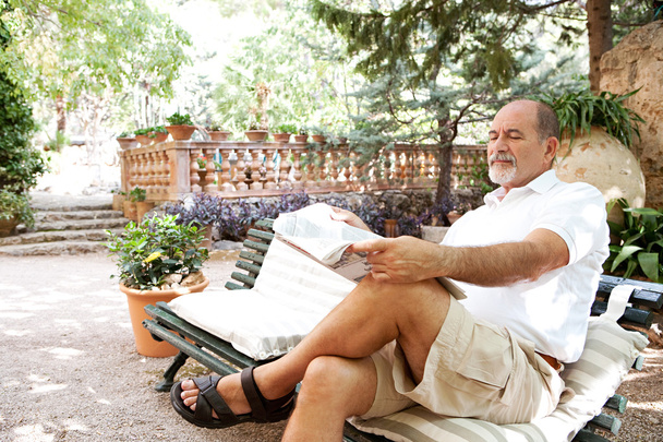 чоловік сидить на лавці і читає газету
 - Фото, зображення