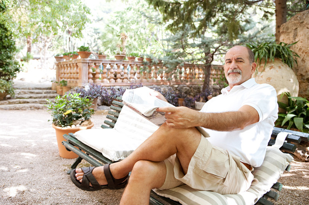 чоловік сидить на лавці і читає газету
 - Фото, зображення