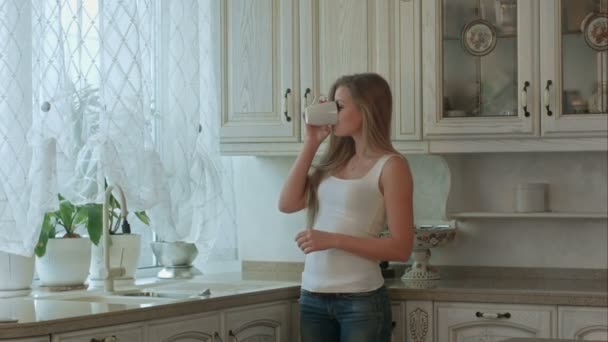 Beautiful girl drinks tea on kitchen at morning - Filmati, video