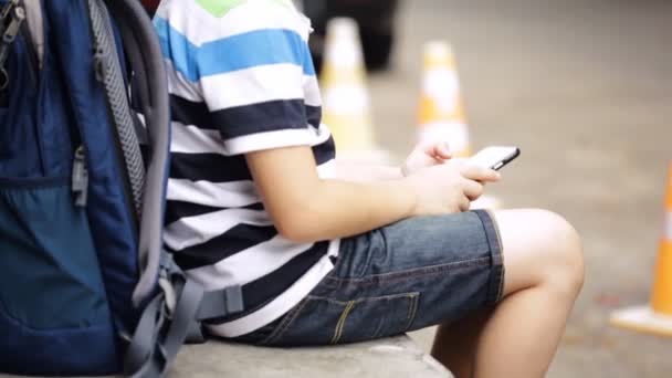 Niño asiático con mochila usando un teléfono celular digital
 - Metraje, vídeo