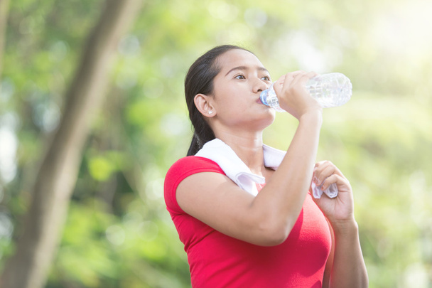 アジアの女性の運動休憩中ミネラル水を飲む - 写真・画像