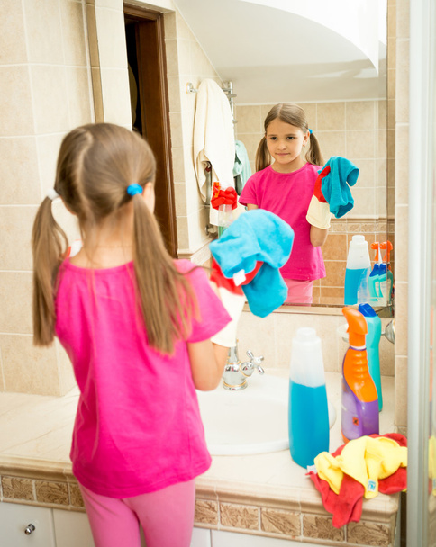 Portret van meisje poets- en reinigingsmiddelen spiegel in de badkamer - Foto, afbeelding