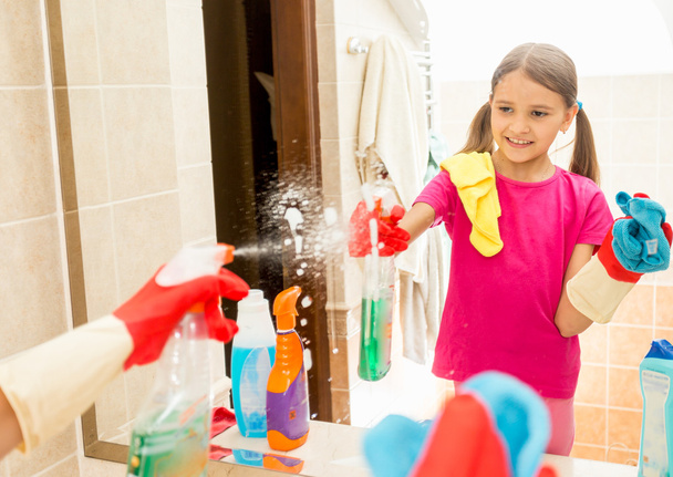 smiling girl cleaning mirror at bathroom with spray and cloth - Foto, Bild