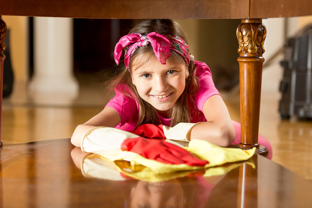 Portrait of smiling girl polishing wooden table with cloth - Photo, Image