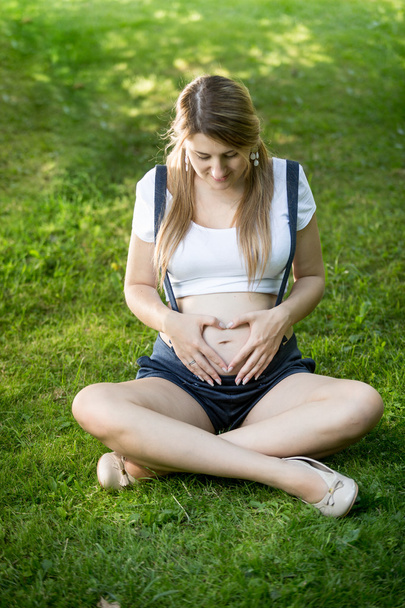 Pregnant woman holding hands at shape of heart on abdomen - Фото, зображення