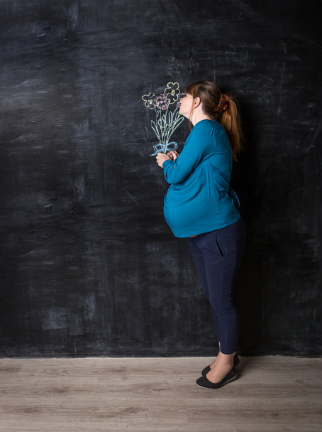 pregnant woman smelling flowers drawn by chalk on big black wall - Фото, зображення