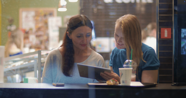 Amigos femeninos hablando y usando almohadilla táctil en la cafetería
 - Metraje, vídeo
