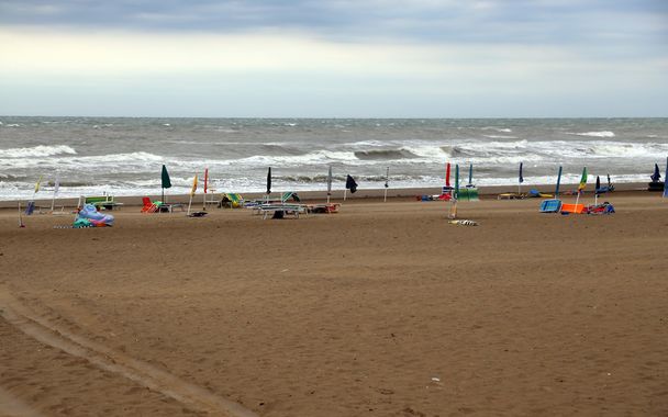 plage avec la mer très rugueuse et de nombreux parasols fermés
 - Photo, image